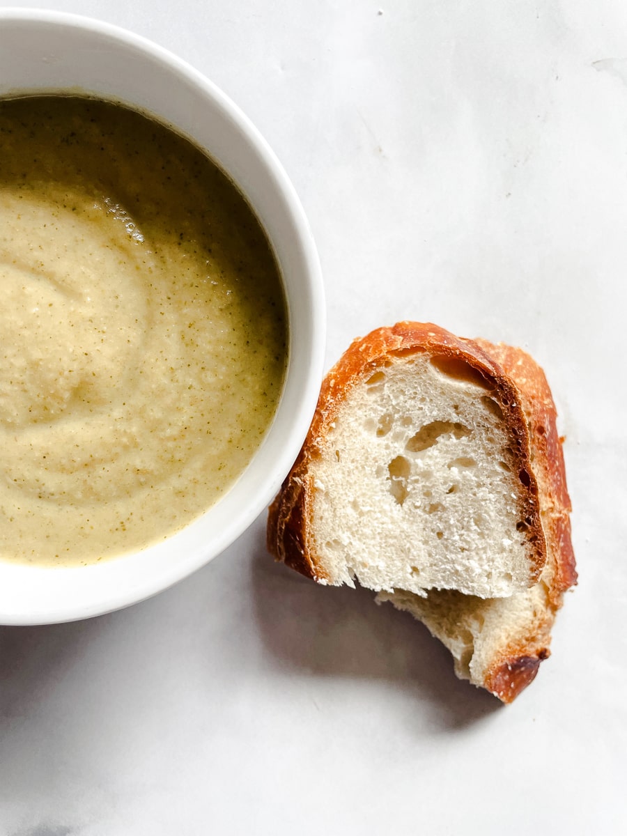 Pieces of bread next to a bowl of vegan broccoli soup.