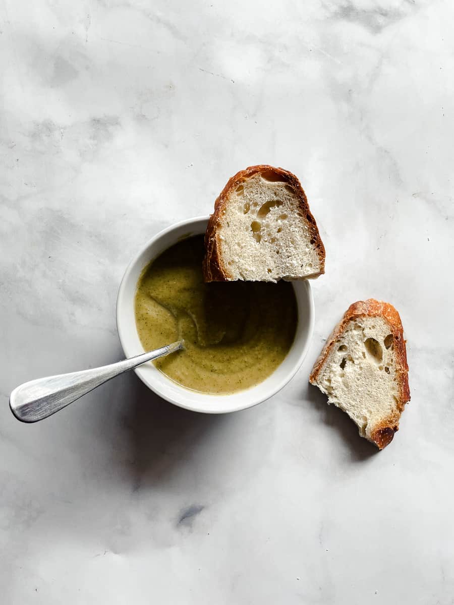 A piece of bread on the rim of a bowl of vegan broccoli soup.
