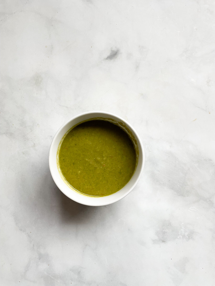 Creamy vegan asparagus soup that's full of fresh vegetable flavors and vibrantly green from plenty of asparagus. A white bowl holds green vegan asparagus soup on a white background.