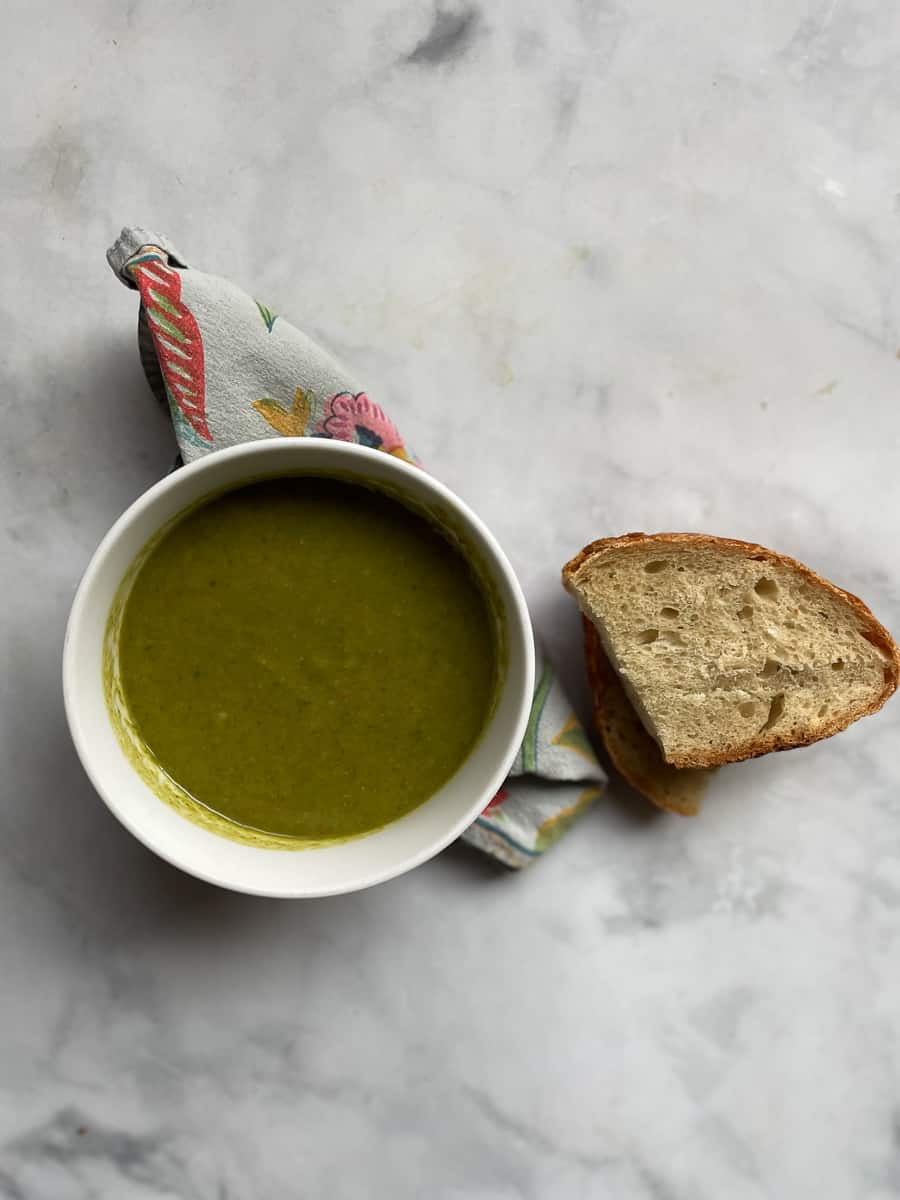 Creamy vegan asparagus soup that's full of fresh vegetable flavors and vibrantly green from plenty of asparagus. A serving of vegan asparagus soup in a bowl with a slice of bread.