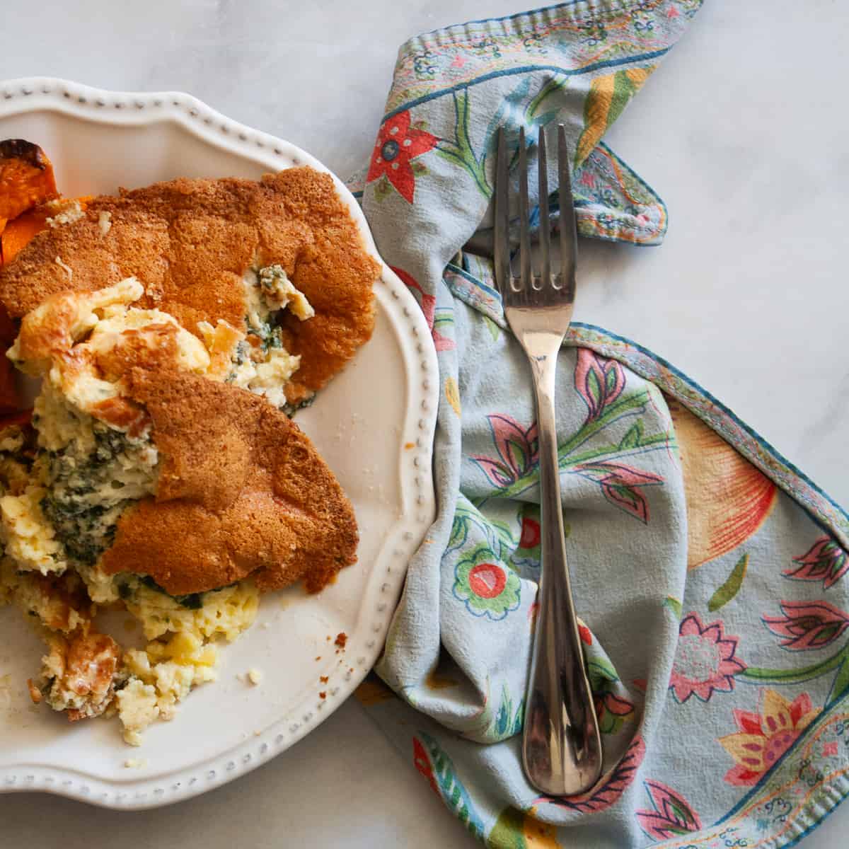 A blue napkin with a fork to the right of a plate of gluten free souffle.