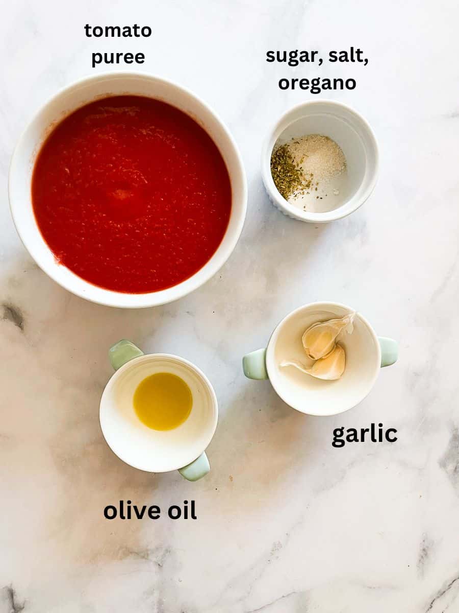 This recipe for super simple tomato sauce is the quickest and easiest tomato sauce you can make from pureed tomatoes plus dried herbs. Ingredients for simple tomato sauce are portioned and labeled: pureed tomatoes, garlic, oregano, salt, sugar, olive oil.