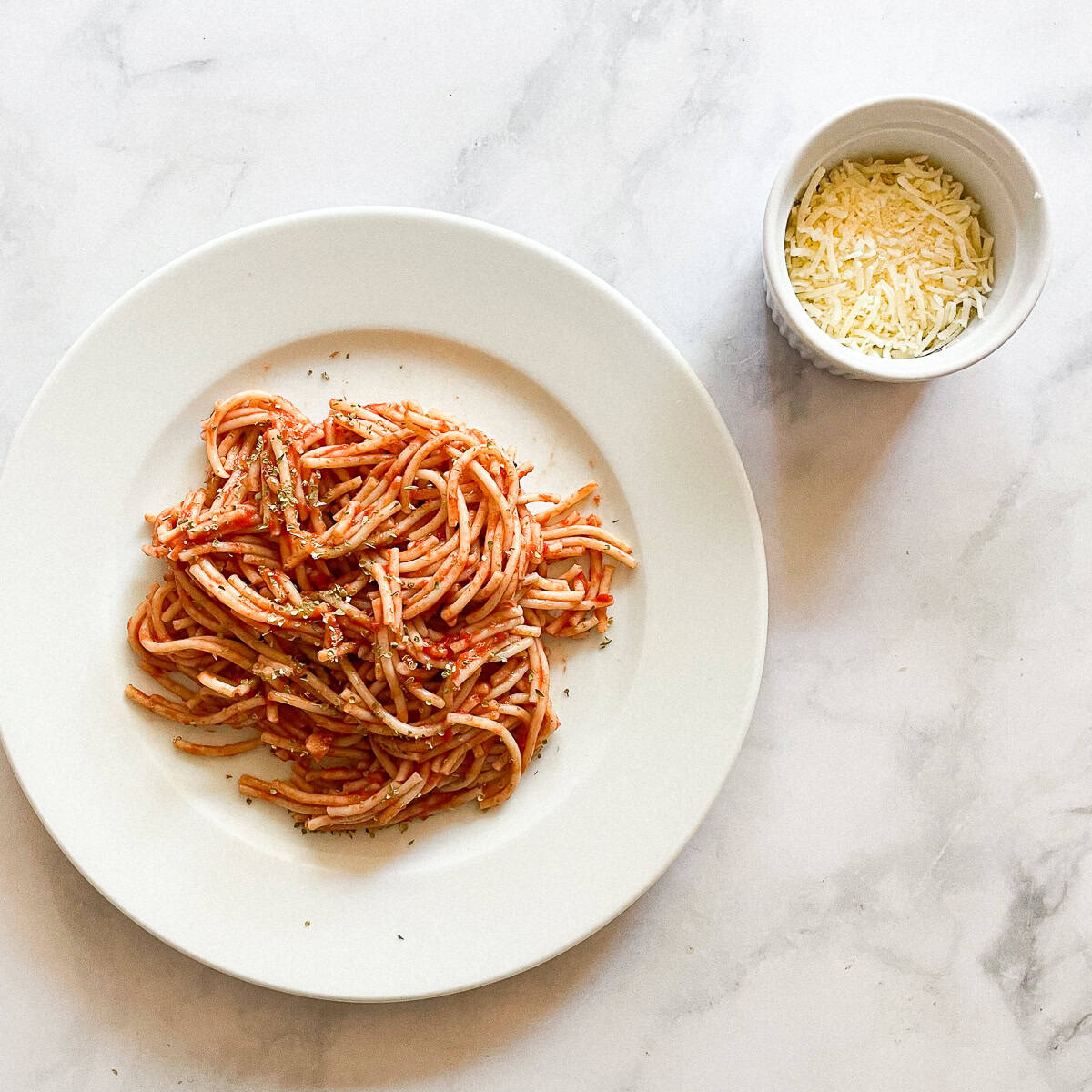 Spaghetti with simple tomato sauce on a plate with a bowl of cheese next to it.
