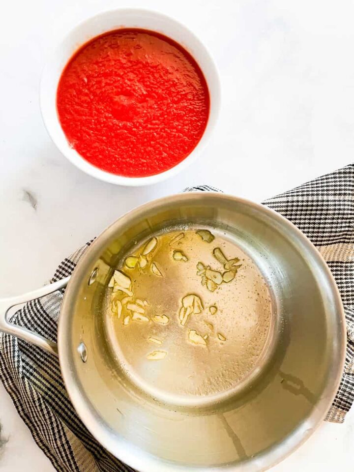 This recipe for super simple tomato sauce is the quickest and easiest tomato sauce you can make from pureed tomatoes plus dried herbs. Garlic cooks in olive oil with pureed tomatoes next to the pot.