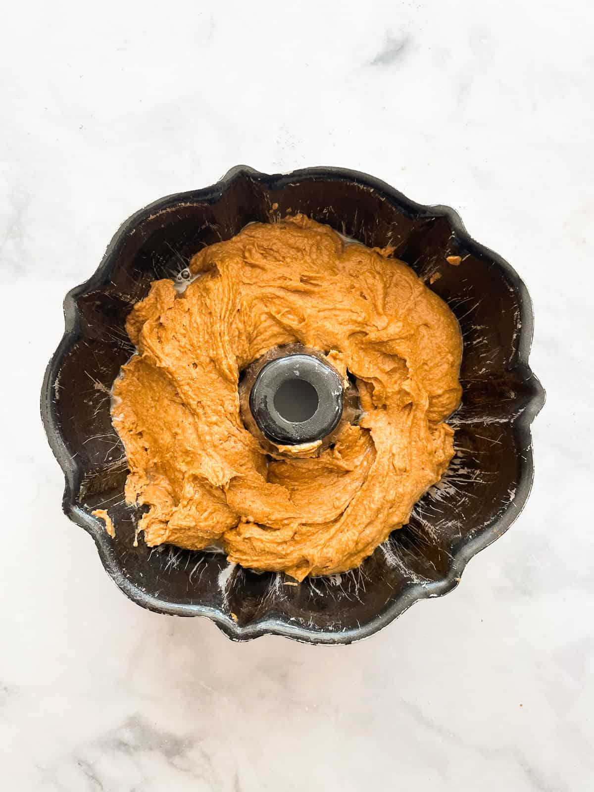 This tender pumpkin spice cake recipe takes a fluffy pumpkin cake and swirls it with a cozy chocolate-spiked cinnamon streusel. Half of pumpkin cake batter in a bundt pan.