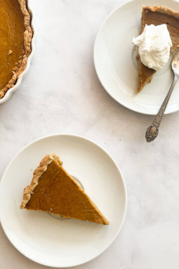 Pieces of homemade pumpkin pie one topped with whipped cream on plates.