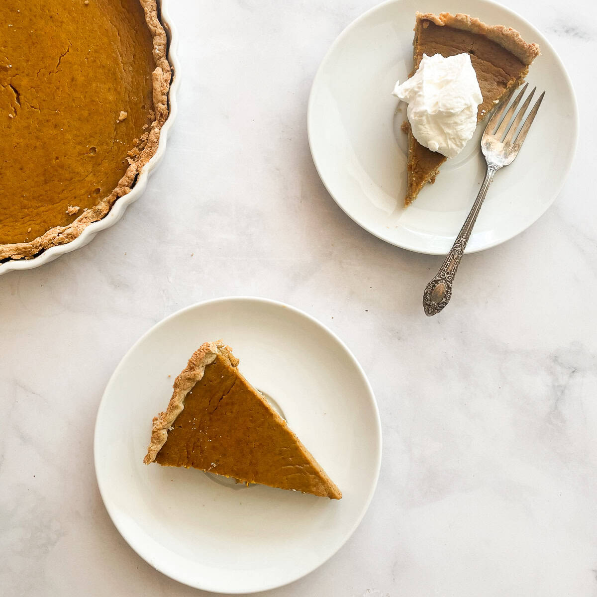 Pieces of homemade pumpkin pie one topped with whipped cream on plates.