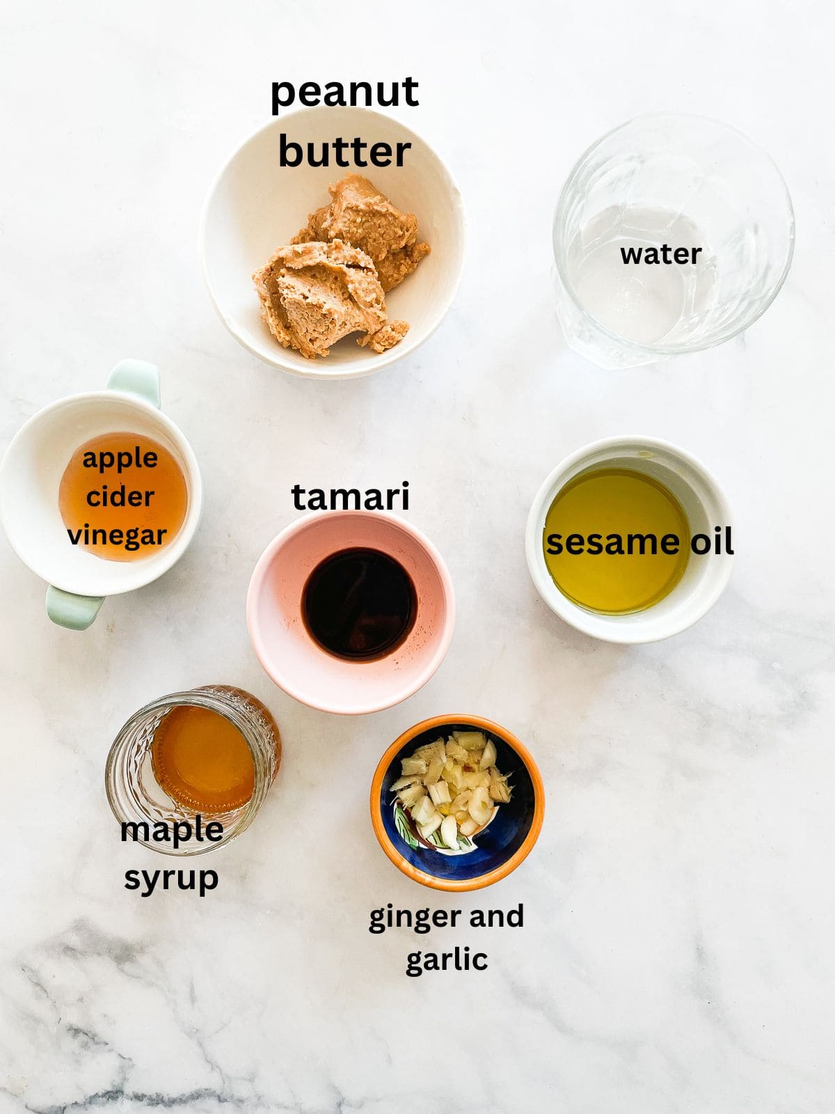Silky smooth ginger peanut sauce features fresh ginger swirled with lots of peanut butter, a little garlic, tamari sauce, and sesame sauce. The ingredients for ginger peanut sauce are text labeled and portioned out.