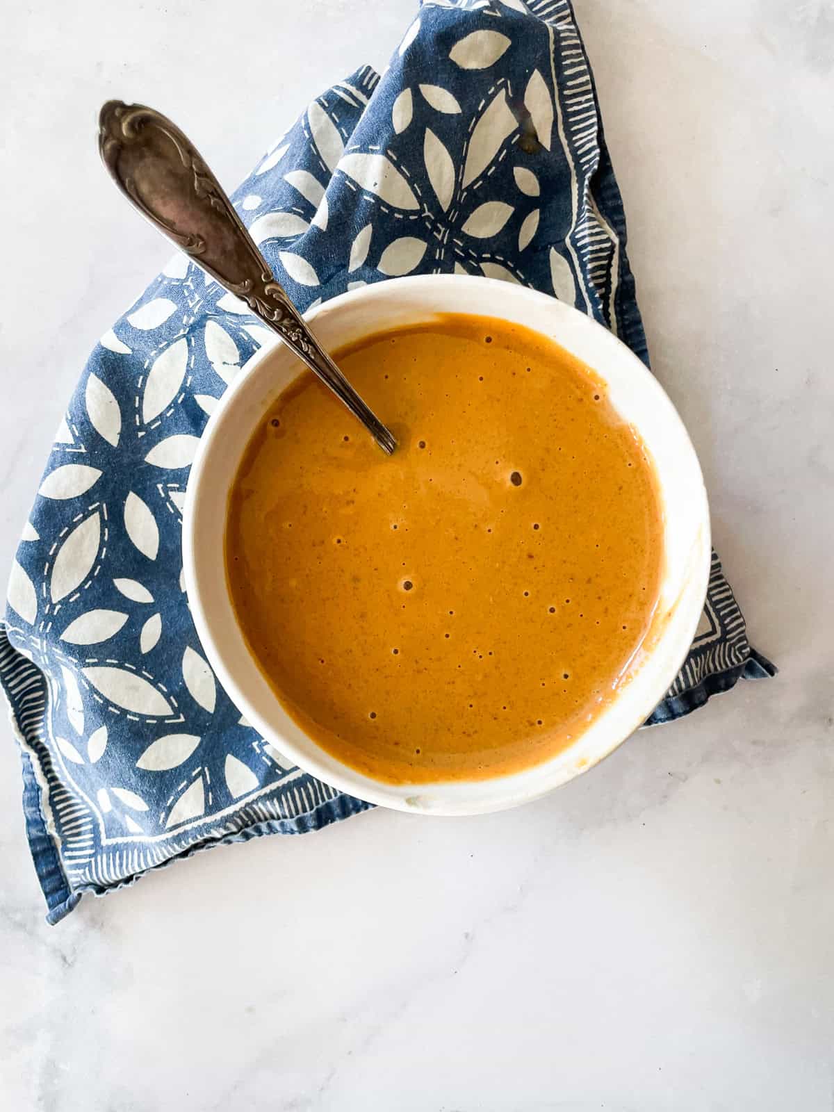 Silky smooth ginger peanut sauce features fresh ginger swirled with lots of peanut butter, a little garlic, tamari sauce, and sesame sauce. A bowl of ginger peanut sauce on a blue napkin.