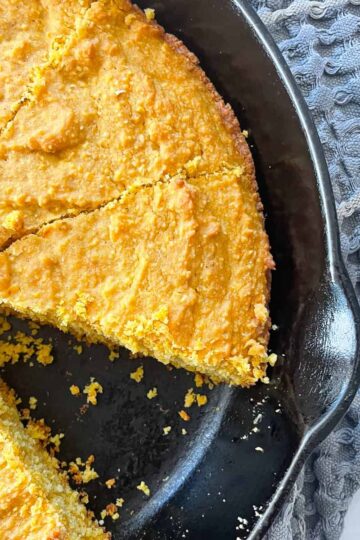 A slice cut out of a pan of pumpkin cornbread.