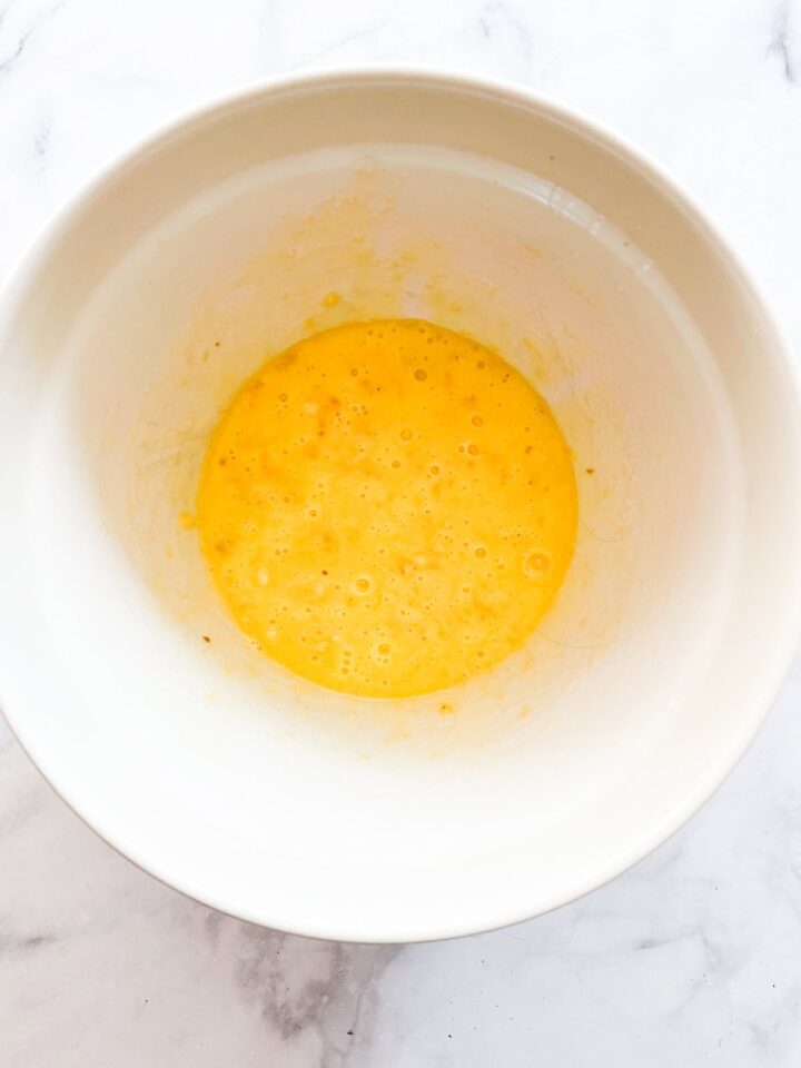 Sweet and moist banana chocolate chunk muffins are studded with big bites of semisweet chocolate for a decadent morning treat. Banana is mixed with egg in a bowl.