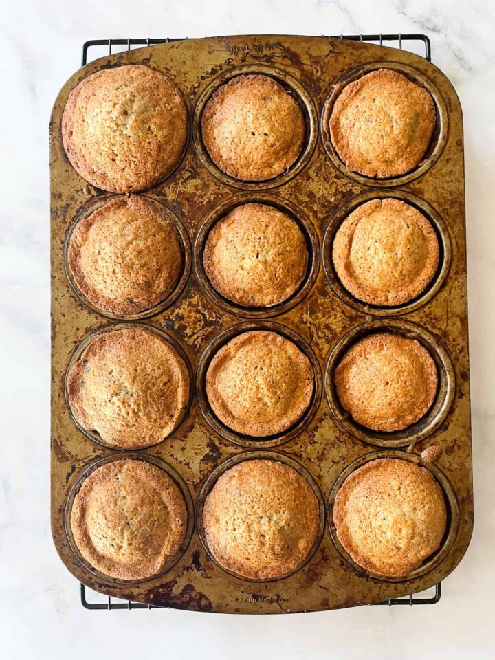 Sweet and moist banana chocolate chunk muffins are studded with big bites of semisweet chocolate for a decadent morning treat. Baked banana chocolate chunk muffins cool in the pan.