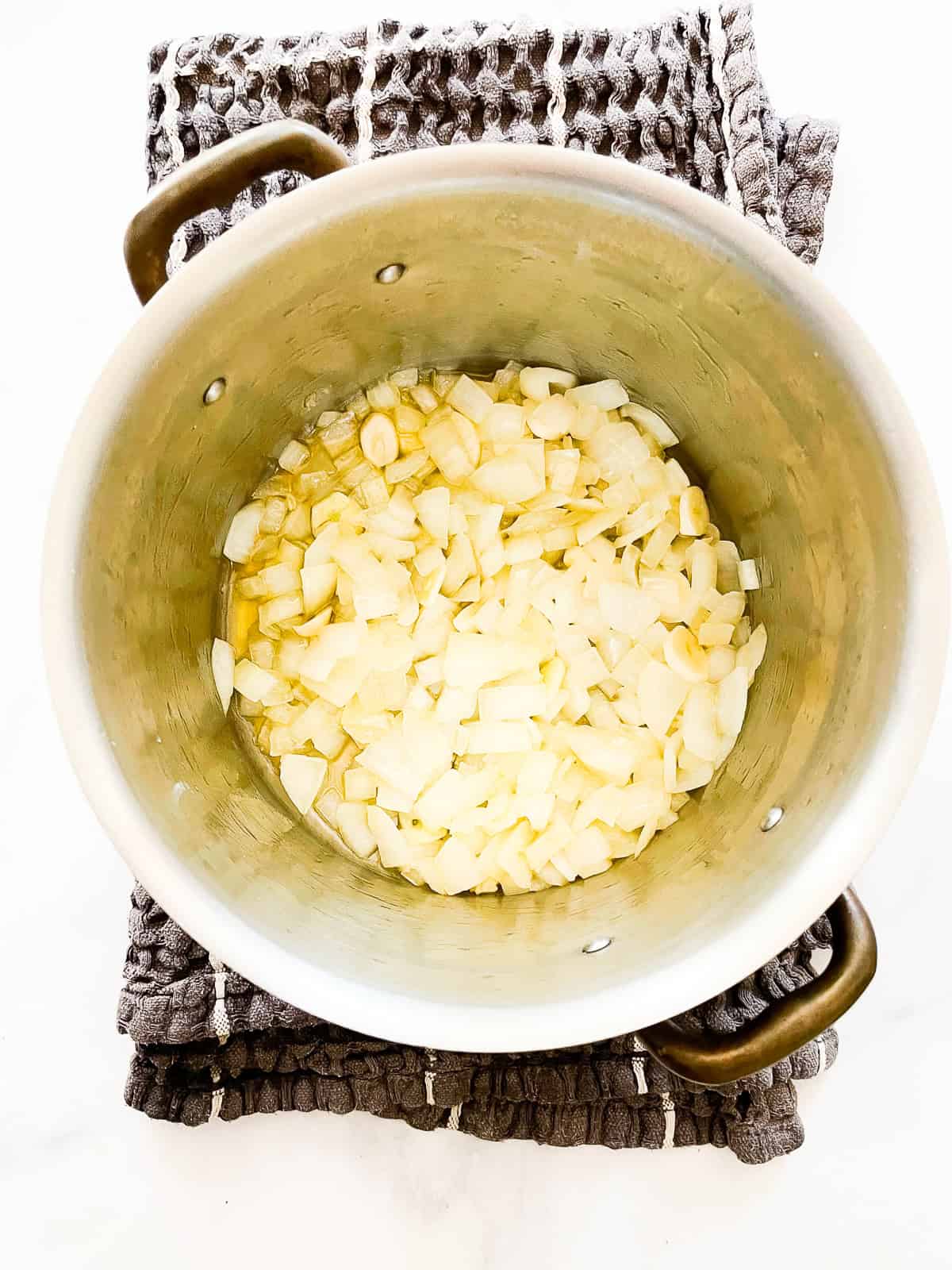 This gluten free butternut squash soup recipe elevates a classic with coconut milk, fresh ginger, and soy sauce. Onions and garlic cook in a pot.