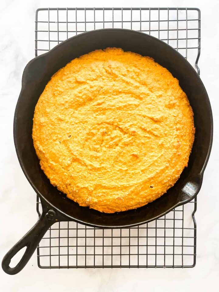 Savory-sweet ultra moist gluten free pumpkin cornbread is a fun and festive holiday side you'll love with soup, stew, and more! Pumpkin cornbread in a cast iron pan cools on a rack.