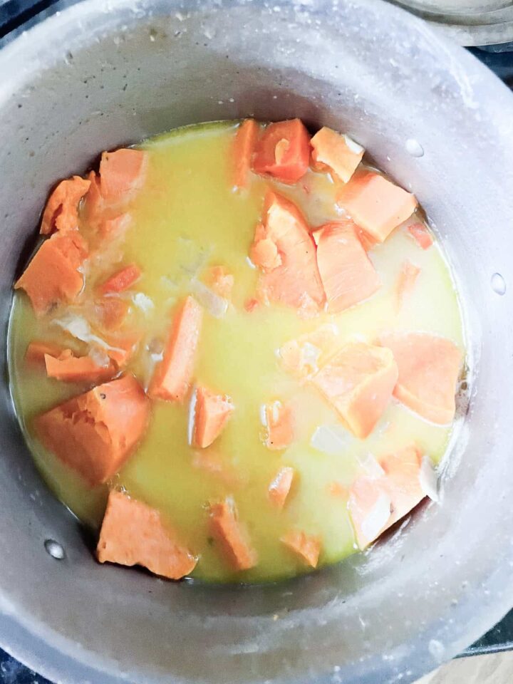 Rich and creamy sweet potato and coconut soup is flecked with fresh ginger and infused with a zingy hint of bright lemon juice. Sweet potatoes cook to softness for soup in a pot.