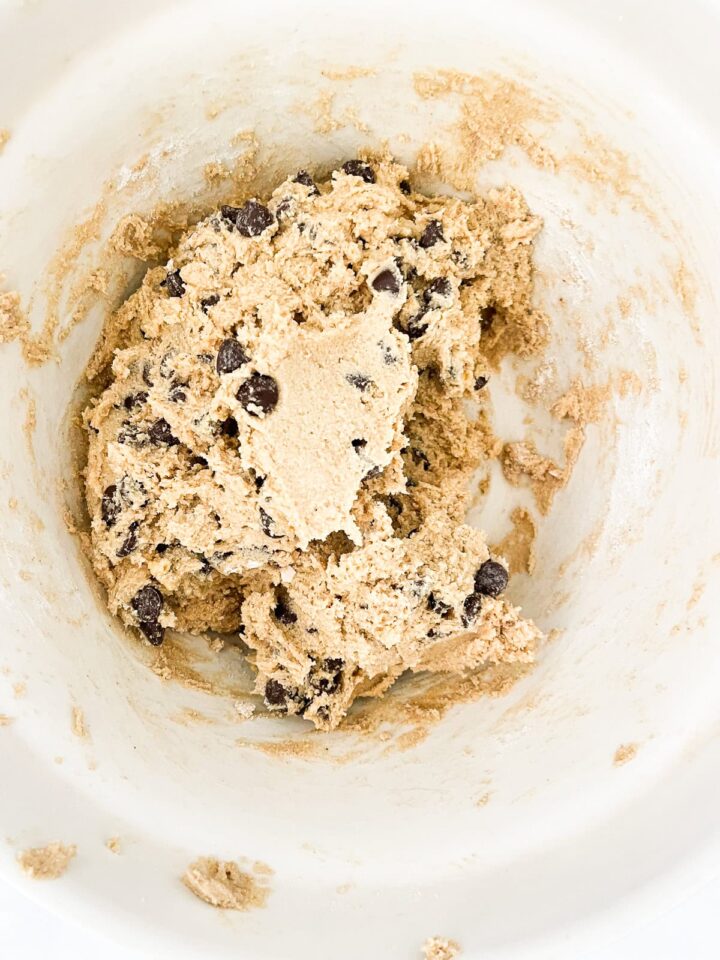 These whole wheat flour chocolate chip cookies will quickly replace your old favorite chocolate chip cookie recipe. They are THE BEST. Chocolate chips are added to cookie dough in a bowl.