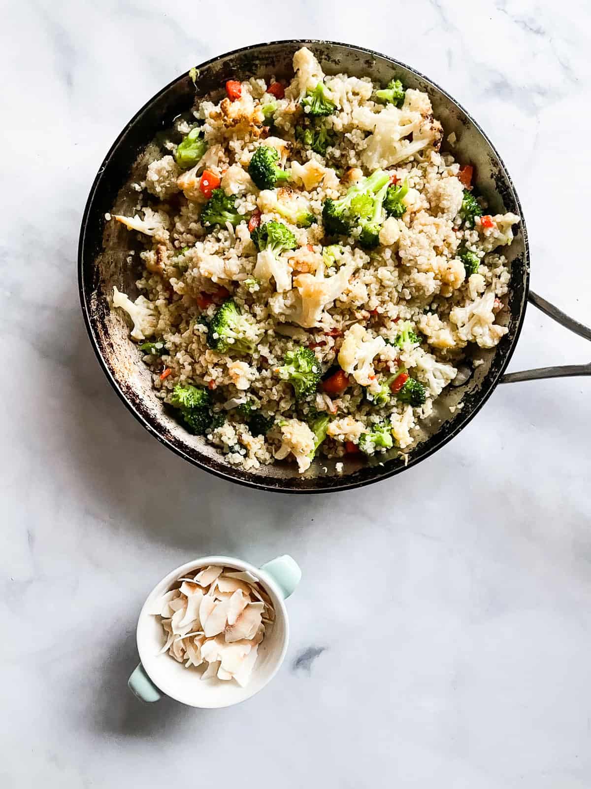 This coconut quinoa with vegetables features coconut-infused, gingery quinoa loaded with carrots, broccoli, and roasted cauliflower. Vegetarian and GF! A dish of toasted coconut next to a skillet of coconut quinoa.