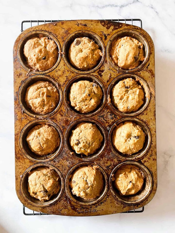 These easy vegan banana muffins are soft, sweet, and easily made gluten-free. Maple syrup and ripe banana stand out. One dozen vegan banana muffins cool in the pan.