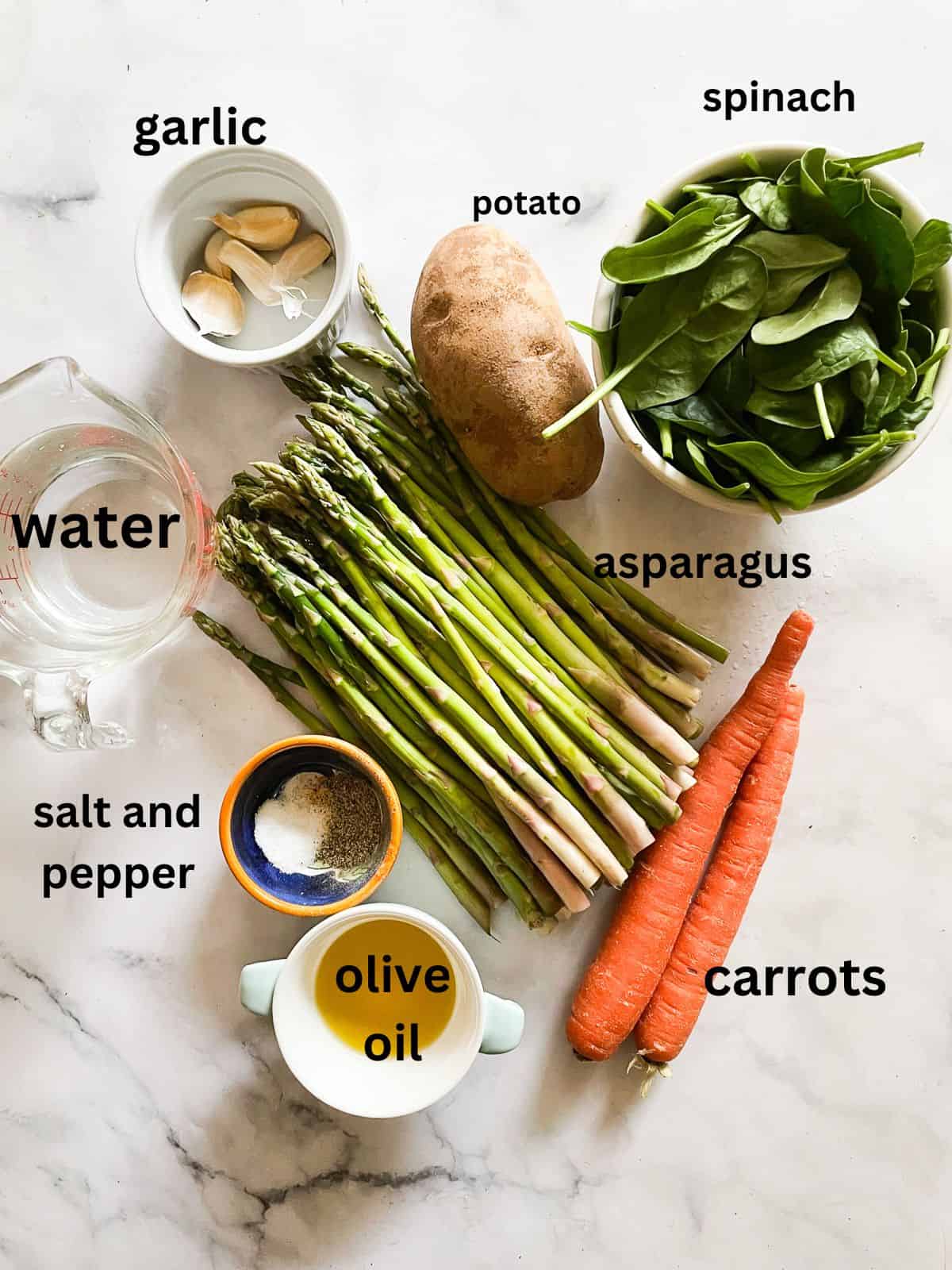 Creamy, cozy asparagus potato soup is crammed with vibrant vegetables like carrots, spinach, and potatoes. Pretty and satisfying! Ingredients for asparagus potato soup are portioned and text-labeled.