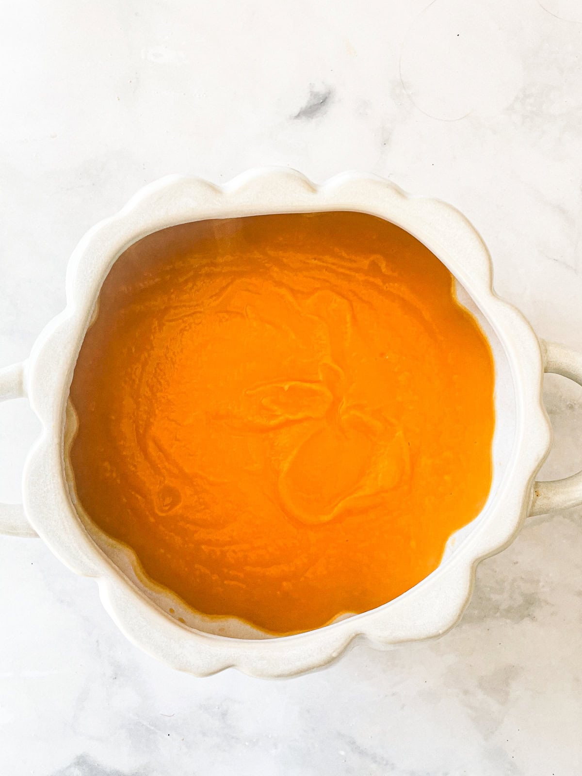 A smooth bowl of butternut squash puree on a white background.
