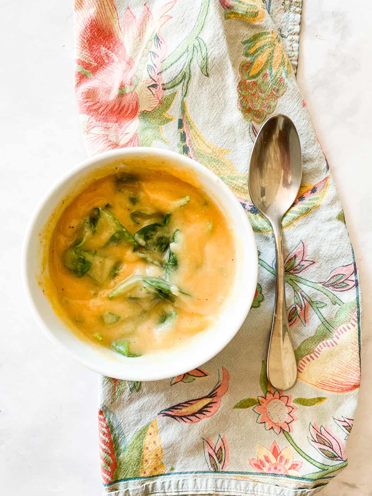 This creamy carrot cauliflower soup is packed with garlic, lots of carrots, and a whole cauliflower. Hearty enough for dinner! A bowl of carrot cauliflower soup with spinach on a napkin.