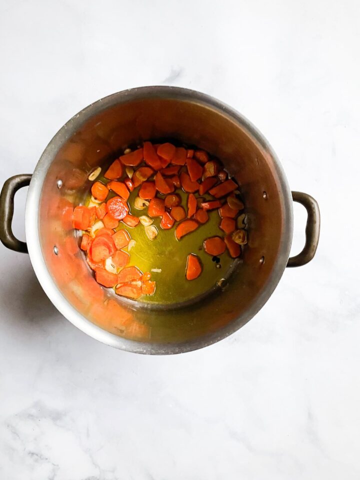 Creamy, cozy asparagus potato soup is crammed with vibrant vegetables like carrots, spinach, and potatoes. Pretty and satisfying! Garlic and carrots cook in a pot.