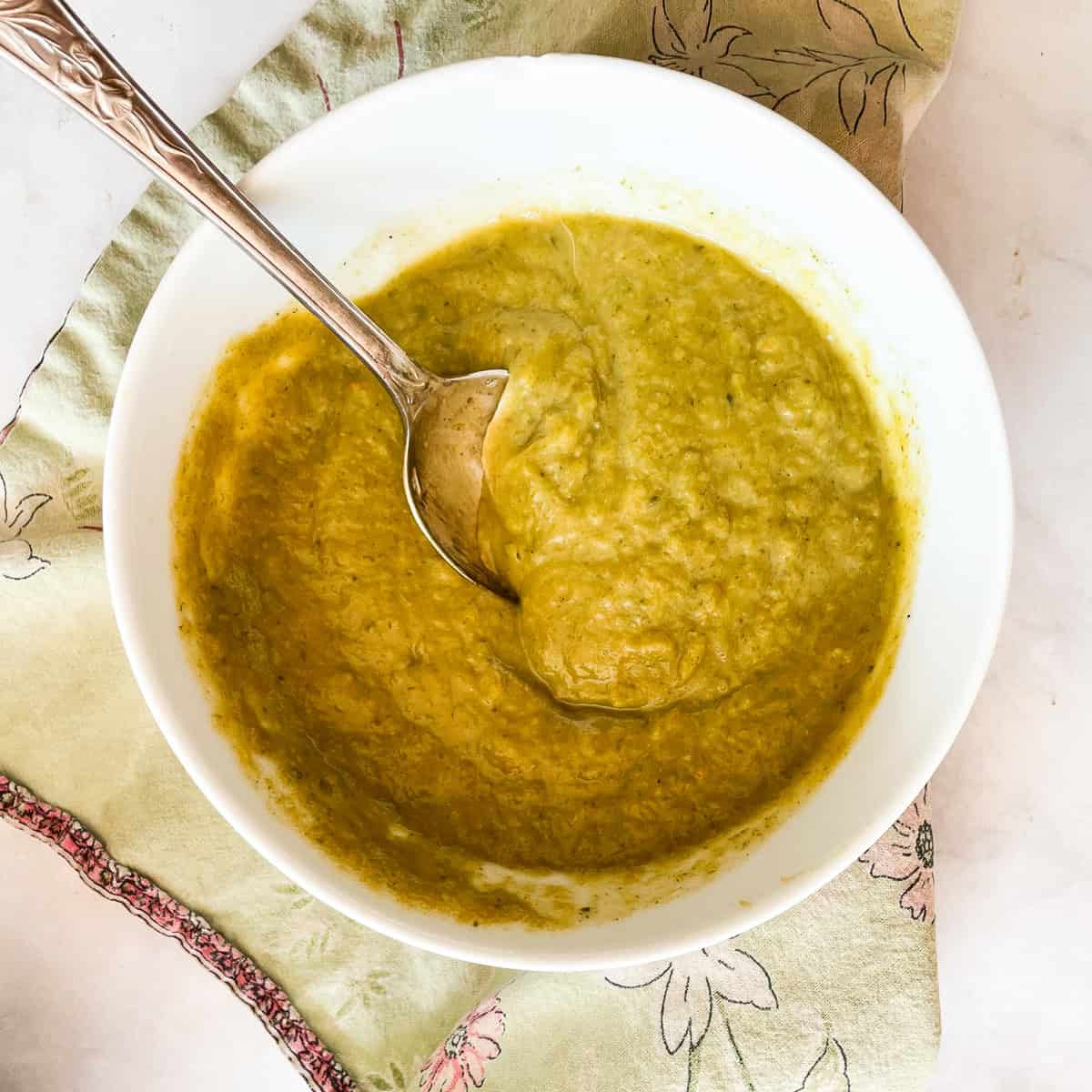 A spoon stirs a bowl of asparagus potato soup.