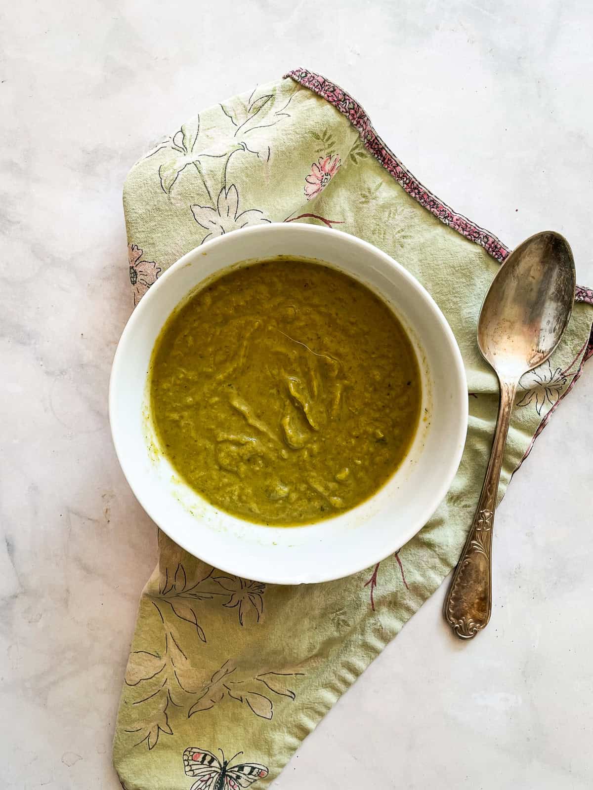 Creamy, cozy asparagus potato soup is crammed with vibrant vegetables like carrots, spinach, and potatoes. Pretty and satisfying! A bowl of asparagus potato soup with a spoon on a green napkin.