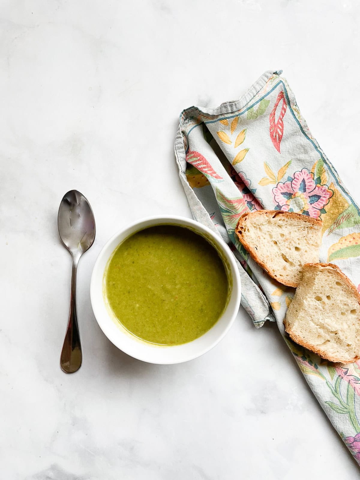 A bowl of vegan asparagus soup with a piece of bread on a napkin and a spoon.