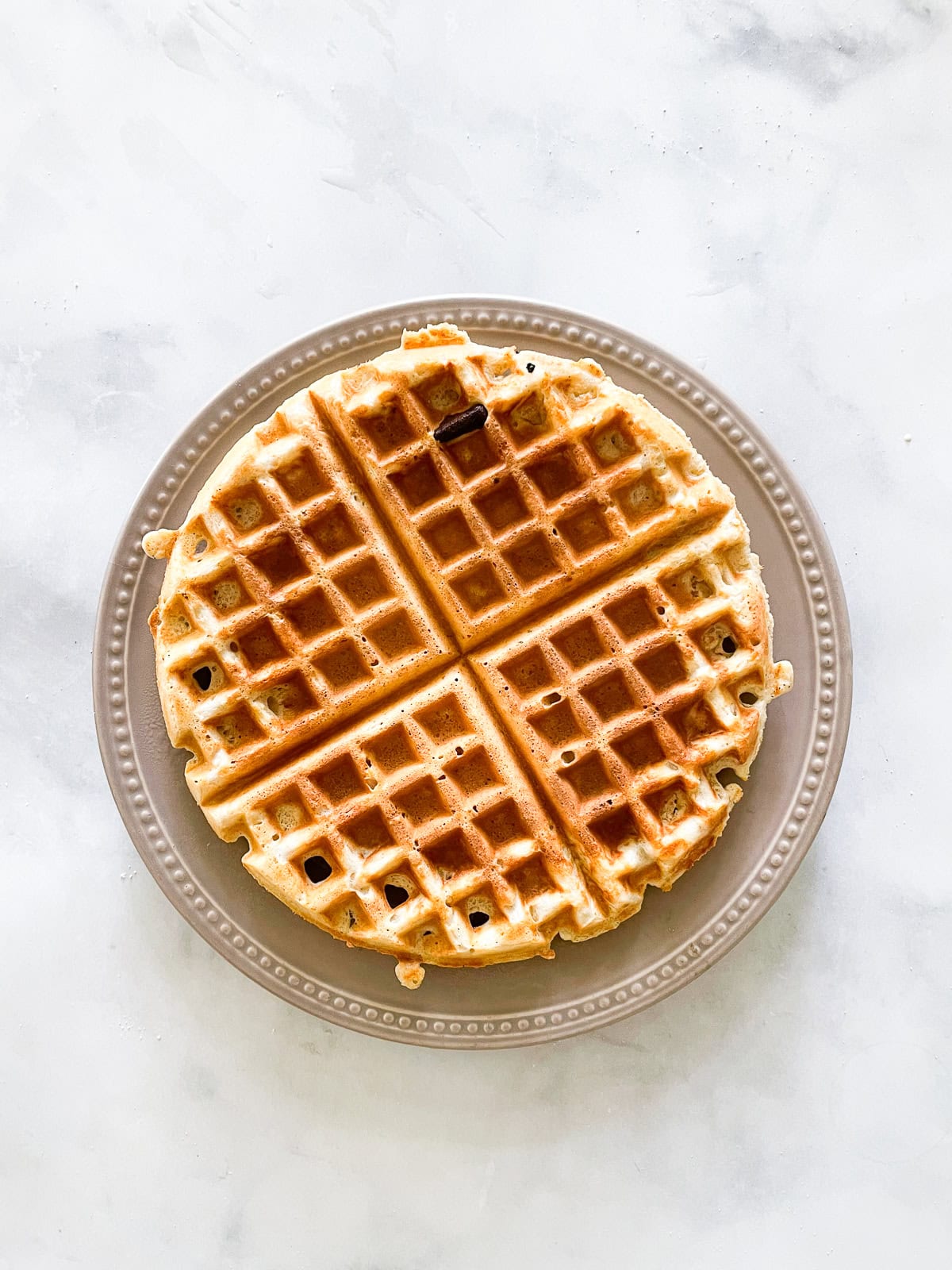 Fluffy whole wheat waffles made with whole grain flour, Greek yogurt, and melted butter! Perfect for a lazy weekend morning. A waffle topped with syrup on a plate.