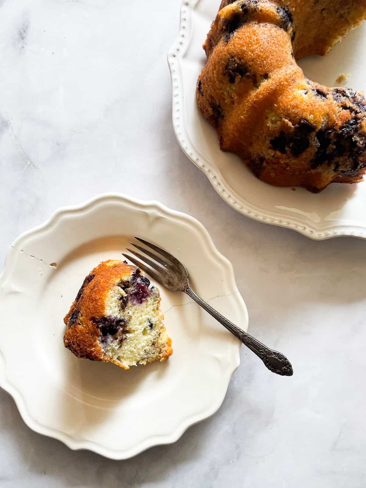 This luscious blueberry yogurt cake is loaded with juicy berries and a sweet cinnamon swirl. Gluten-free option included! A slice of plated blueberry yogurt cake and the cake next to it.