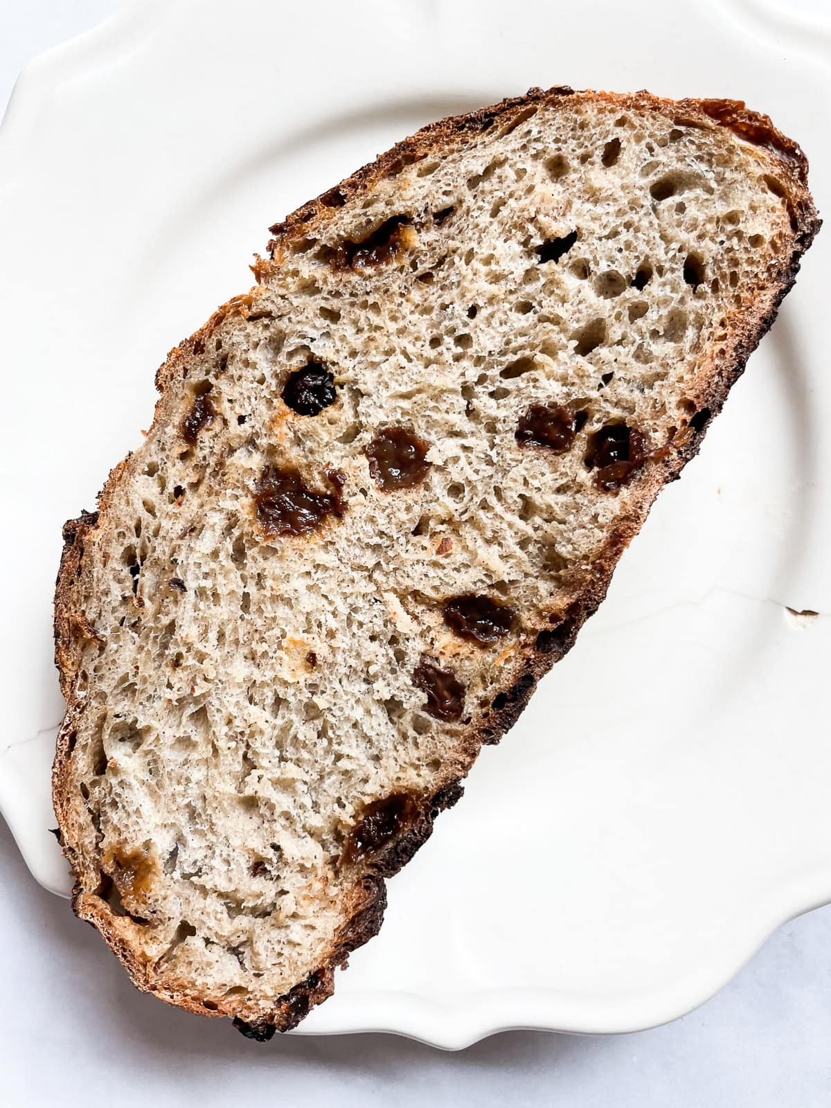 Easy no knead cinnamon raisin bread benefits from a long overnight rise and a bake in a hot Dutch oven! A fantastic recipe for beginners. A slice of cinnamon raisin bread on a plate.