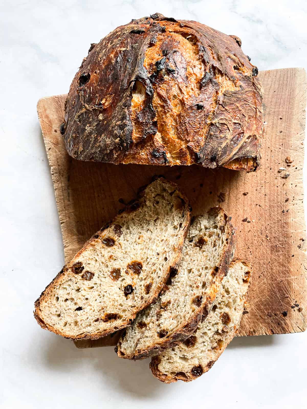 Easy no knead cinnamon raisin bread benefits from a long overnight rise and a bake in a hot Dutch oven! A fantastic recipe for beginners. A loaf of cinnamon raisin bread on a wooden cutting board cut into slices.