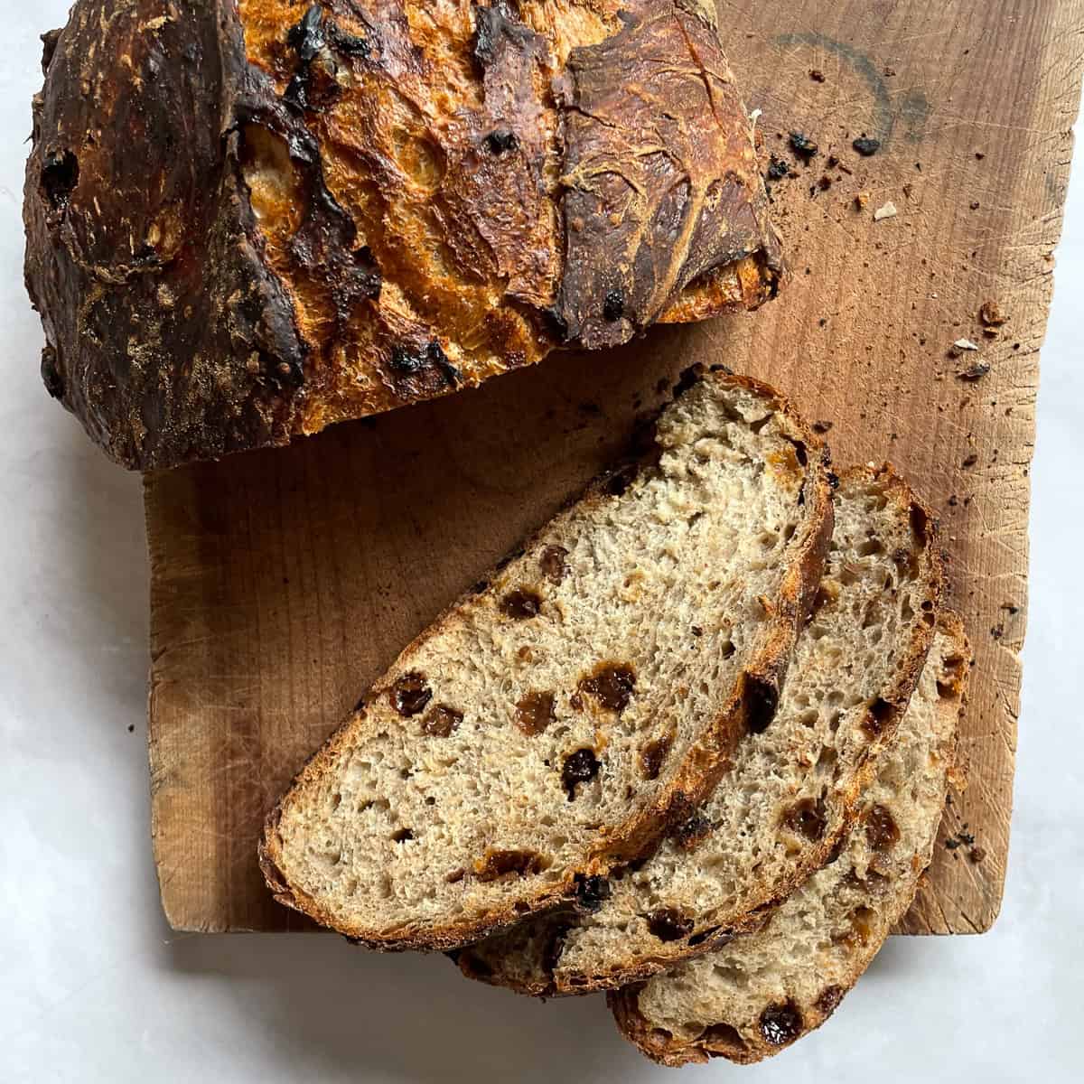A loaf of cinnamon raisin bread on a wooden cutting board cut into slices.