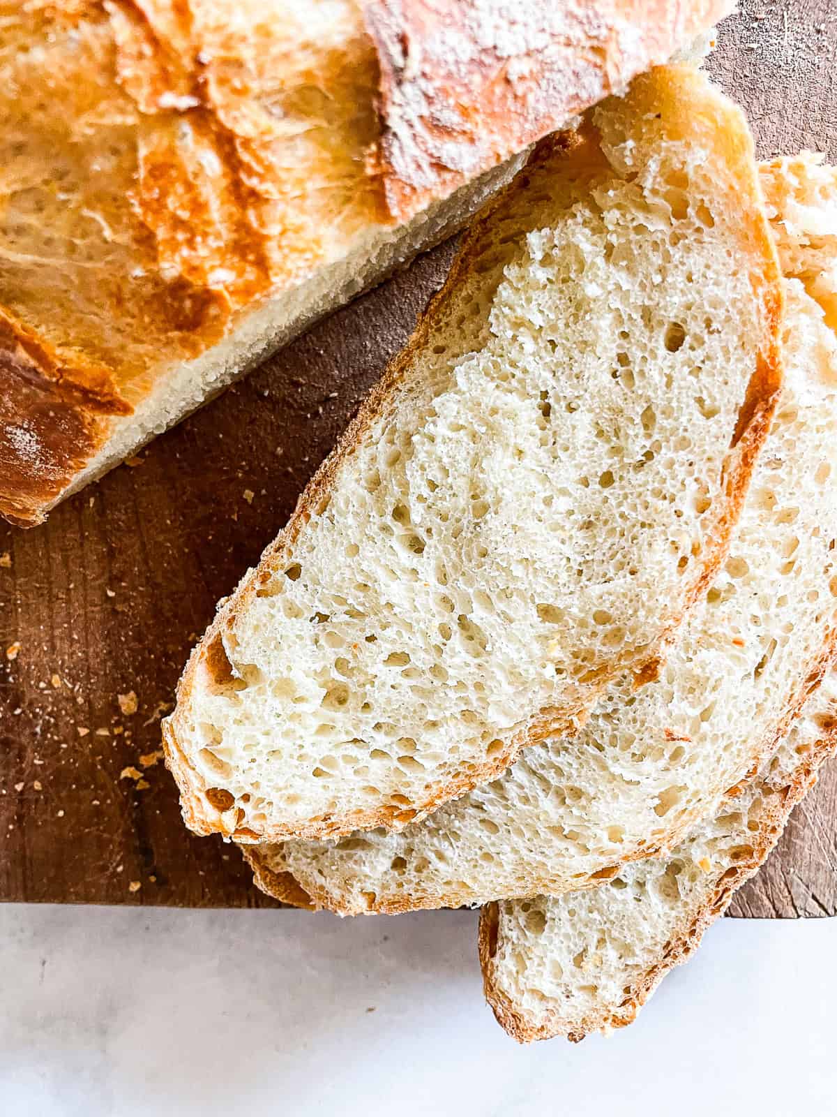 Easy dutch oven bread is my version of the beloved no knead bread recipe. Made with 4 ingredients and baked to golden perfection. Slices of easy dutch oven bread cut from the loaf.