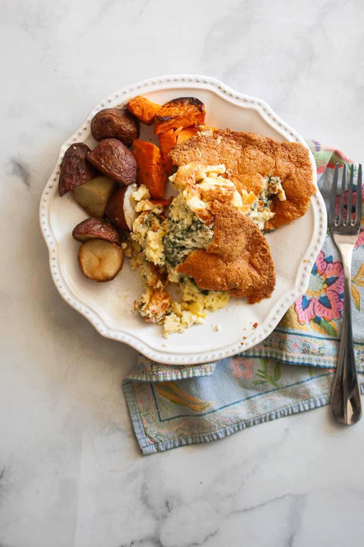 A plate of gluten free souffle on a napkin. Roasted veggies accompany it.