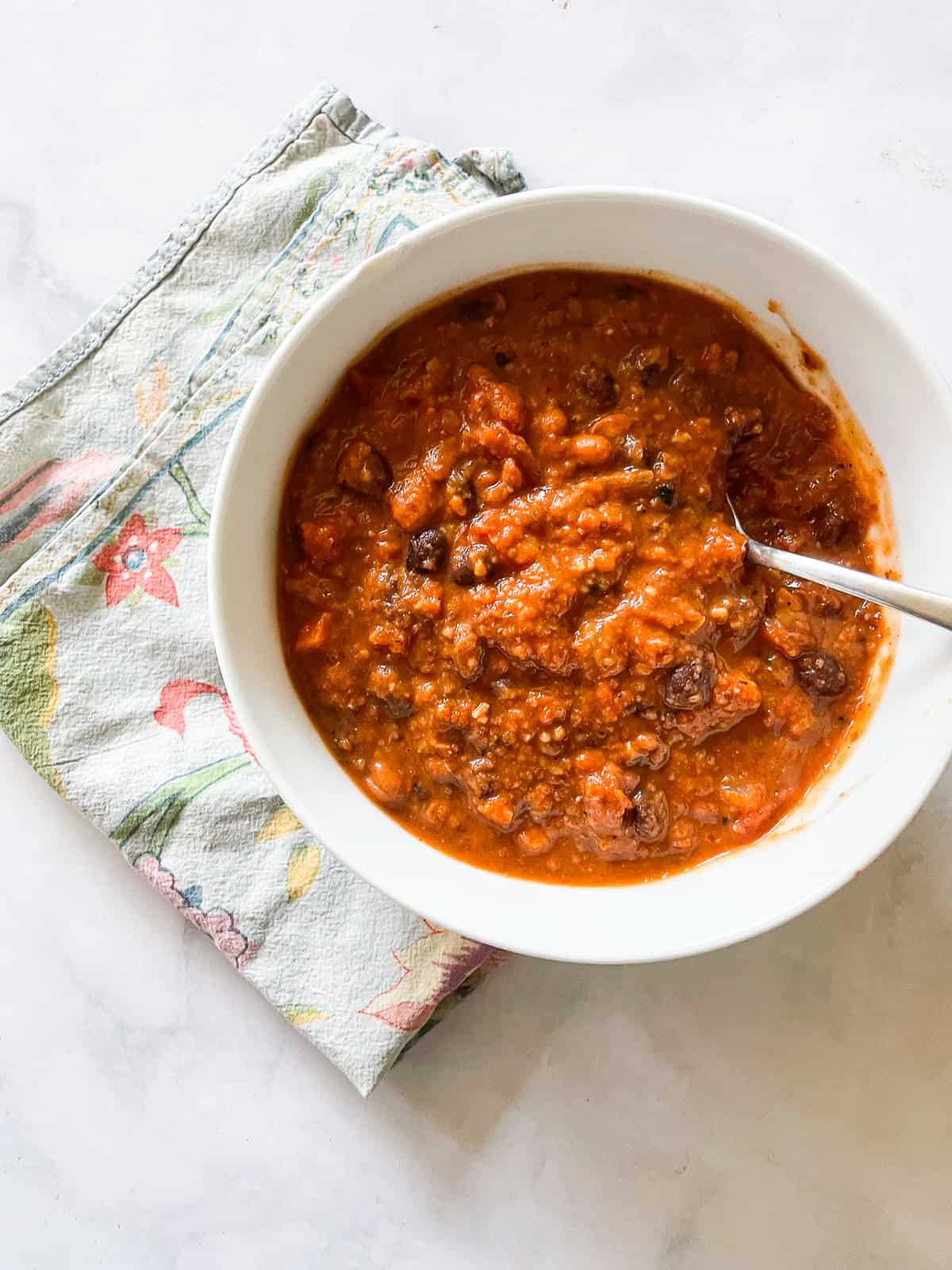 A bowl of gluten free chili on a napkin with a spoon in it.