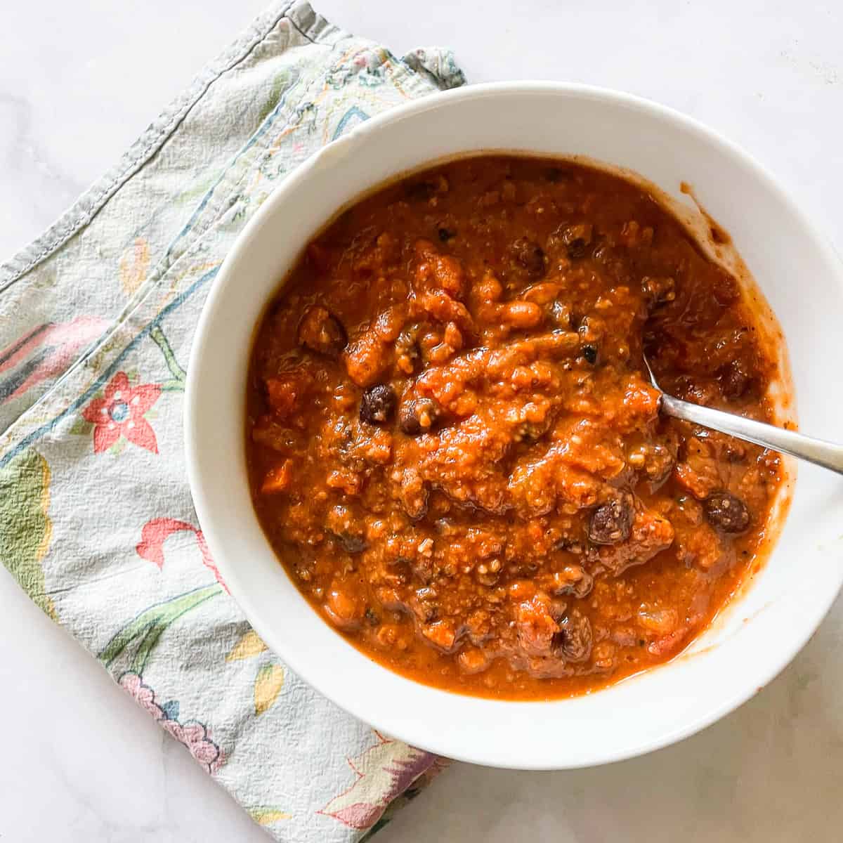 A bowl of gluten free chili on a napkin with a spoon in it.