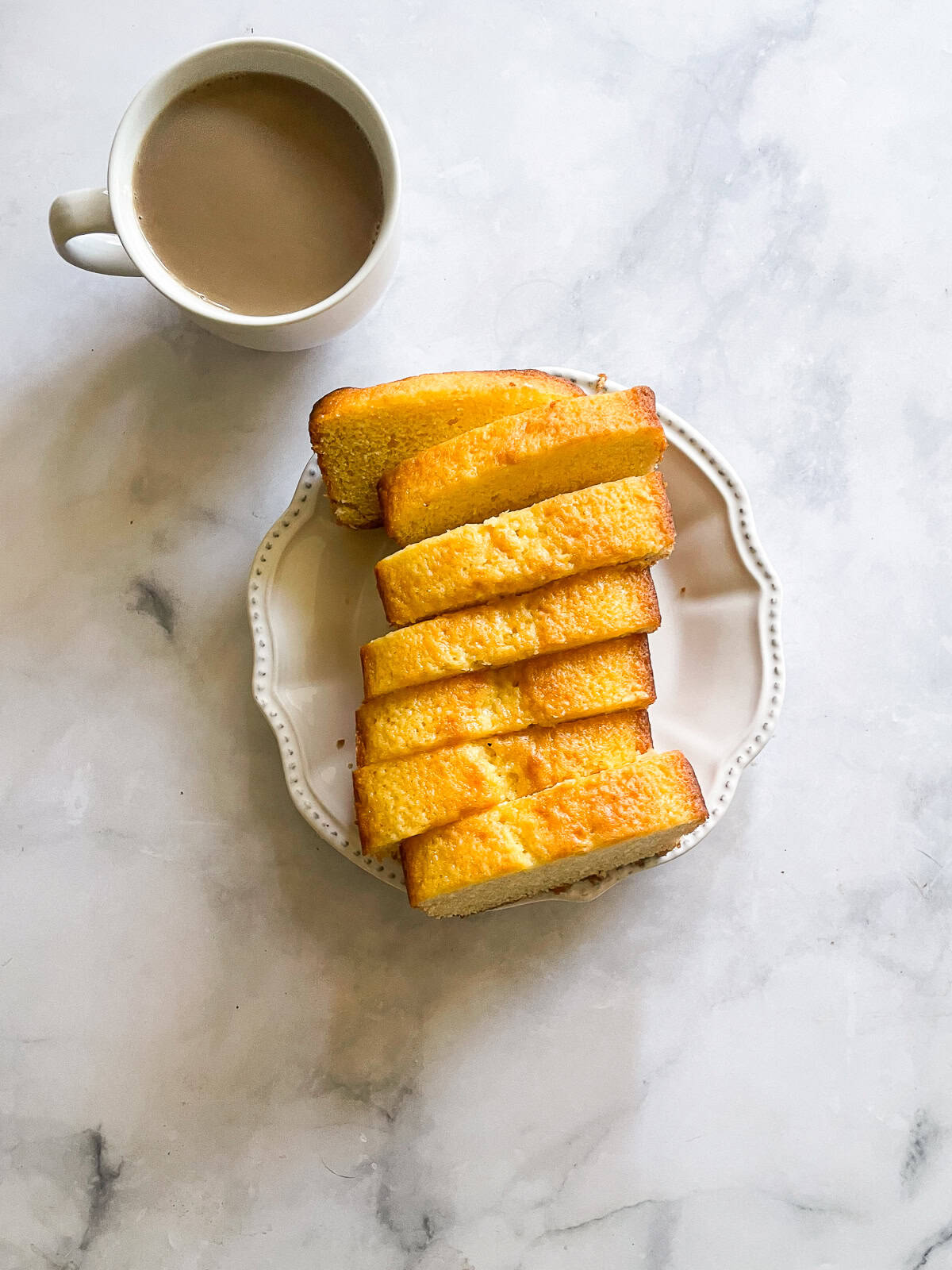 This classic French-inspired lemon yogurt cake is a reliable one-bowl recipe that always turns out perfectly. A cup of coffee next to a plate of lemon yogurt cake.