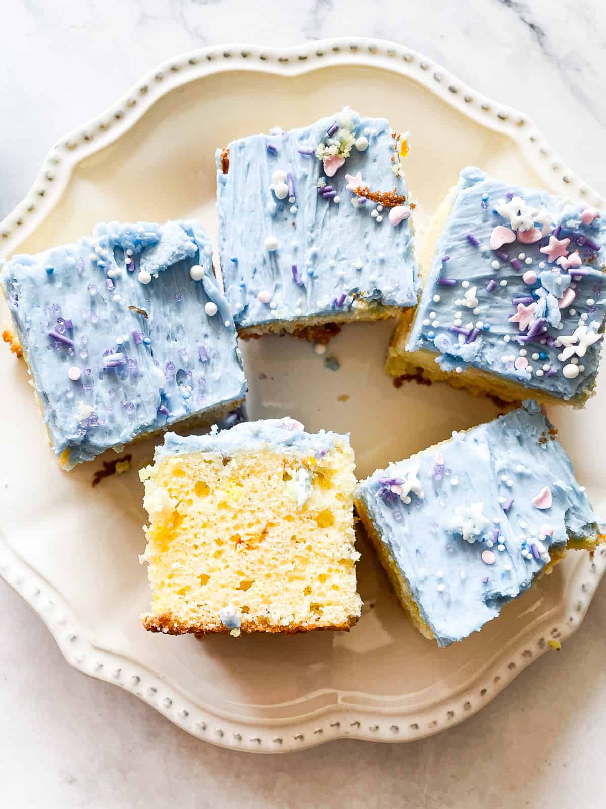 These adorable unicorn bars are perfect for a kid's birthday party! A buttermilk funfetti sheet cake is topped with blue icing and plenty of sprinkles. A unicorn bar turned on its side on a plate with more bars.