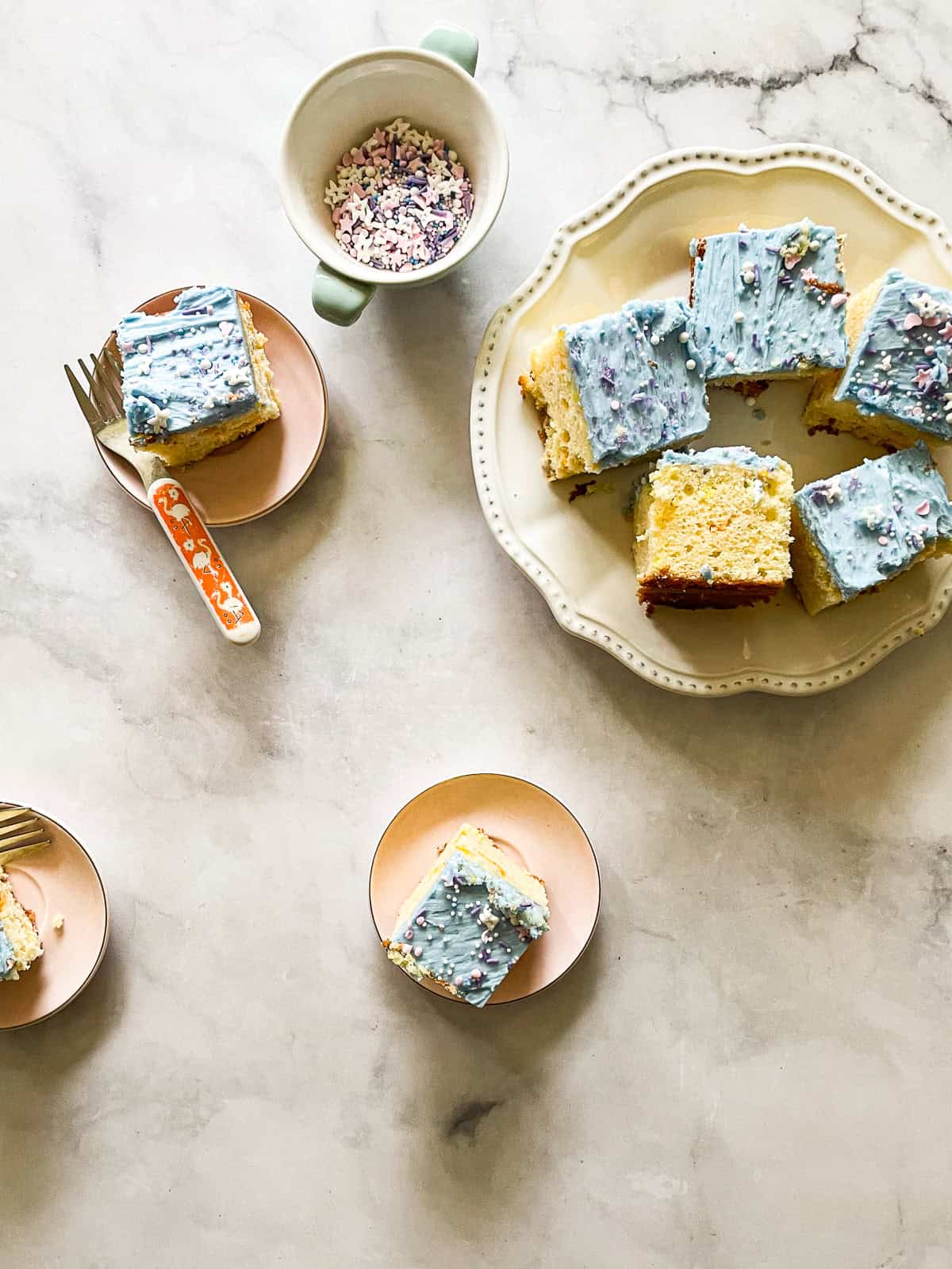 A plate of unicorn bars next to a bowl of sprinkles and more bars,