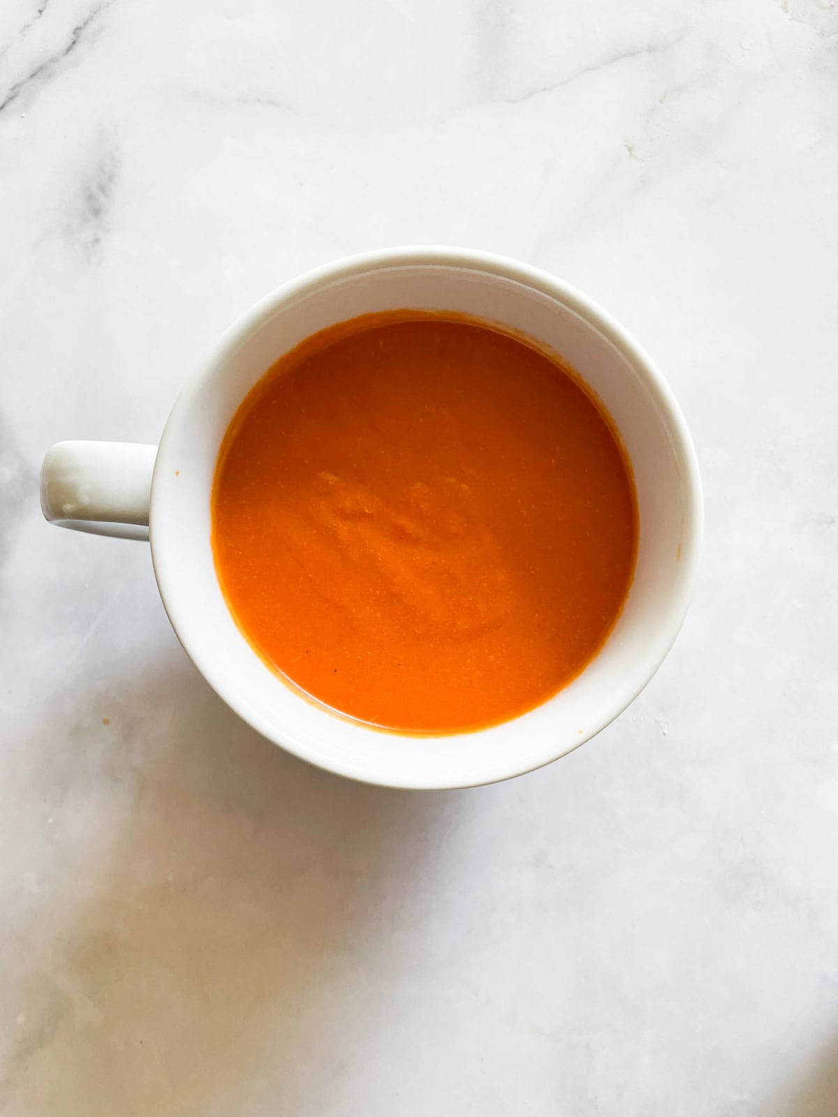 Rich and velvety smooth vegetarian cream of tomato soup is the definition of comfort food—perfect on its own or paired with grilled cheese. A white cup of cream of tomato soup.