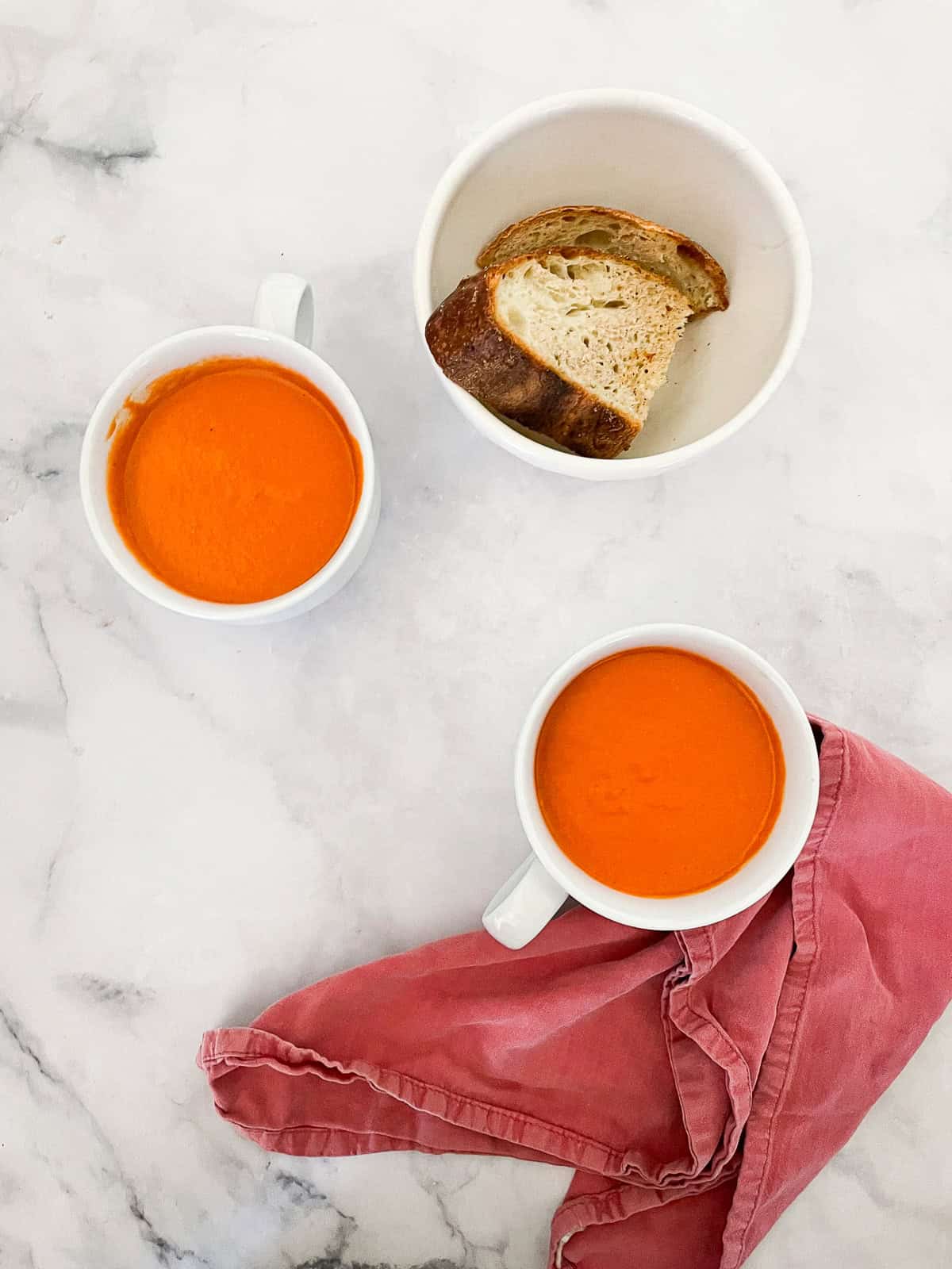 Rich and velvety smooth vegetarian cream of tomato soup is the definition of comfort food—perfect on its own or paired with grilled cheese. Cups of vegetarian cream of tomato soup with a bowl of bread.