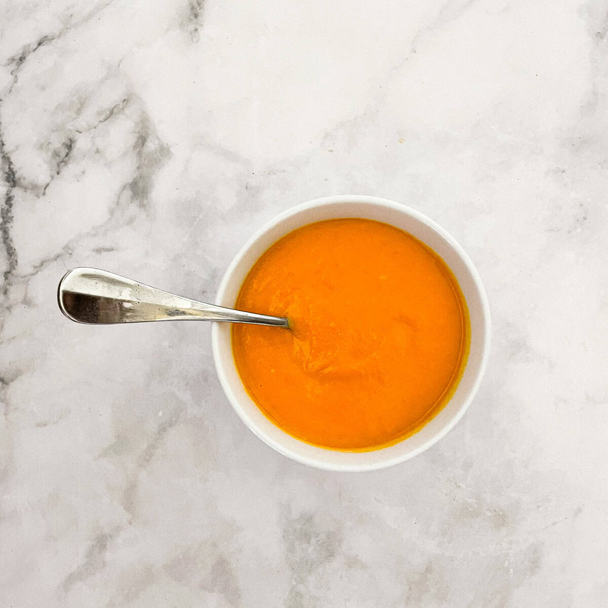 A small bowl of carrot & coconut soup with a spoon.