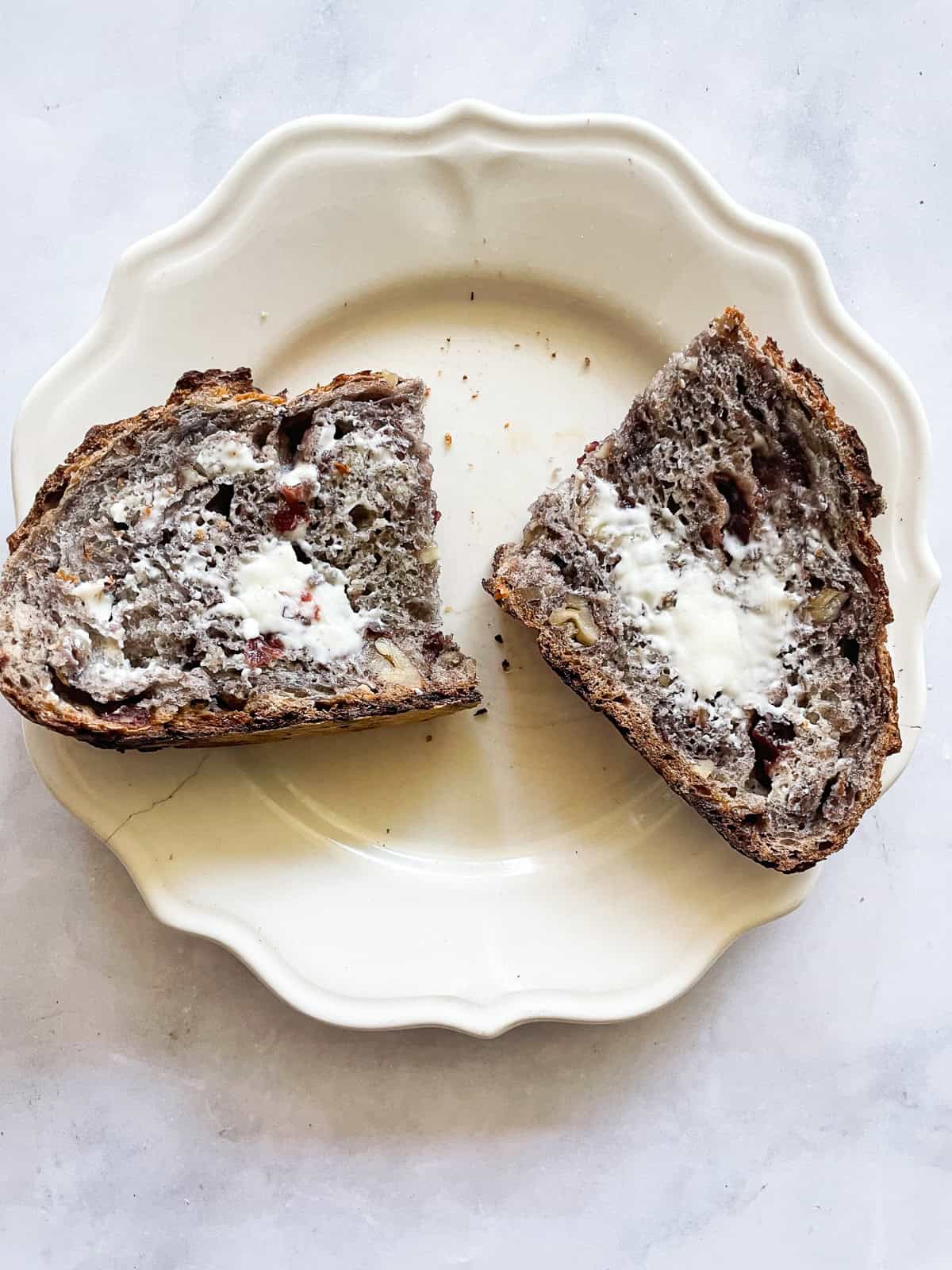 No-knead cranberry walnut bread is studded with sweet-tart dried fruit and crunchy nuts. An easy homemade version of a bakery loaf. A slice of cranberry walnut bread cut in half and topped with butter.