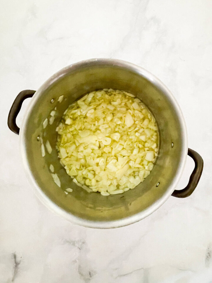 Creamy carrot & coconut soup made with simple ingredients. Naturally vegan, gluten-free, and perfect for weeknight dinners or meal prep. Onions and garlic sauteed in a pot.