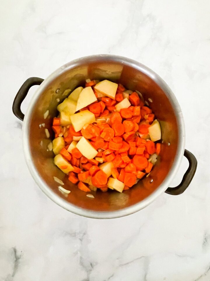 Creamy carrot & coconut soup made with simple ingredients. Naturally vegan, gluten-free, and perfect for weeknight dinners or meal prep. Carrots and potatoes are added to onions and garlic in a pot.