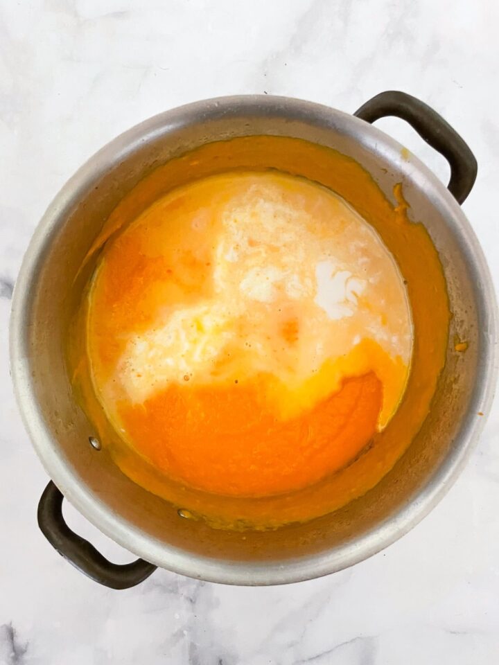 Creamy carrot & coconut soup made with simple ingredients. Naturally vegan, gluten-free, and perfect for weeknight dinners or meal prep. Coconut milk is added to a pot of carrot soup.