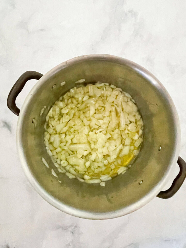 Creamy carrot & coconut soup made with simple ingredients. Naturally vegan, gluten-free, and perfect for weeknight dinners or meal prep. Chopped onions and garlic are added to a soup pot.