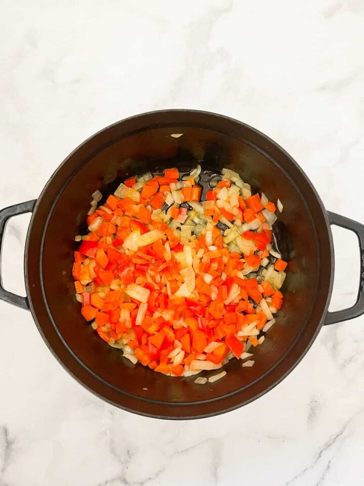 Dig into a hearty bowl of vegetarian white chili that features tender white beans swirled in a rich tomatoey base. Onion and peppers sautee in a pot.